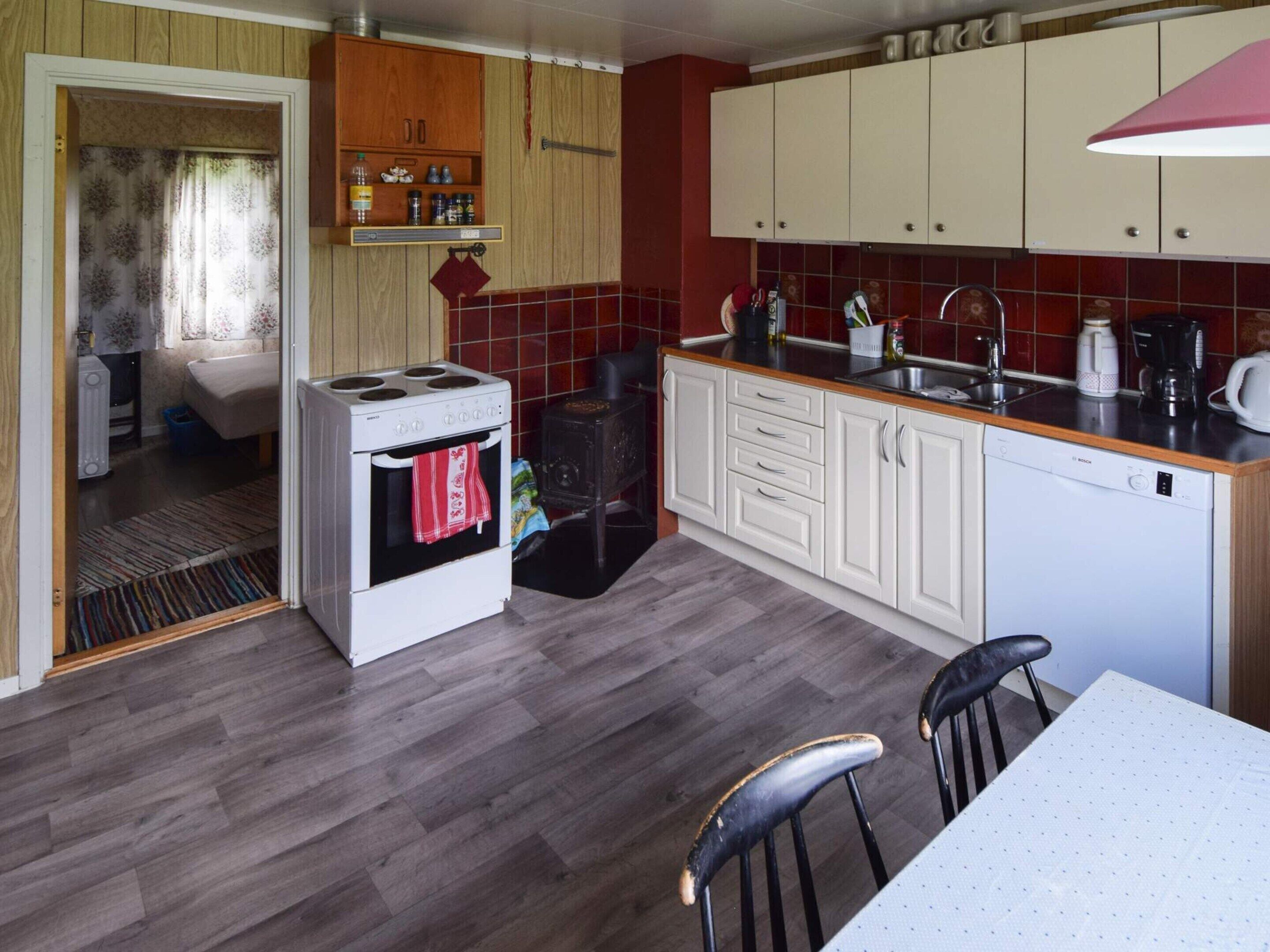 Een kleine keuken met een fornuis, oven en vaatwasser. Er is een eethoek met een tafel en stoelen. De keuken heeft houten kastjes en een betegelde spatwand.