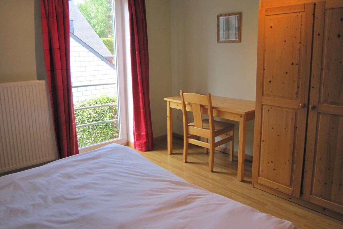 A bedroom with a bed, a wooden desk, a chair, and a wardrobe.
