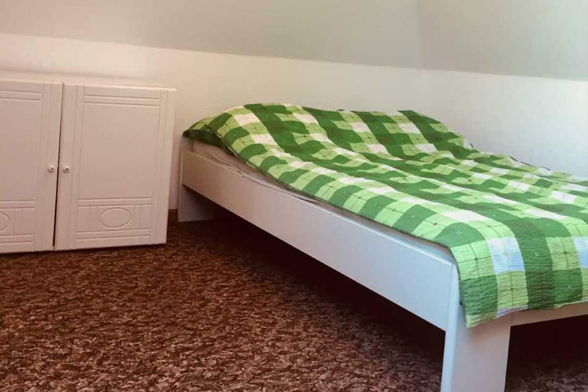 Una stanza piccola con un letto singolo, un letto bianco e una coperta a quadri verdi.