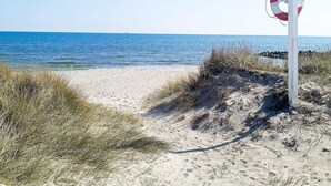 A beach with a lifebuoy attached to a pole, clear blue water, and sandy dunes.