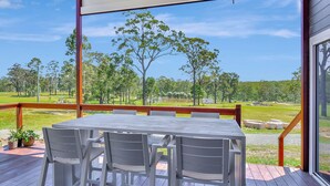 An outdoor deck with a table and chairs, overlooking a grassy area with trees and a body of water. - Two for Joy Estate. Sleeping 12, 2 Cottages (North Rothbury)
