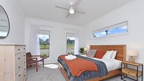Une chambre avec un grand lit, un bureau et une chaise. On y trouve un ventilateur de plafond, une fenêtre et une vue sur l’extérieur.