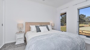 Een slaapkamer met een bed, nachtkastjes, een plafondventilator en een groot raam met uitzicht op de omgeving.