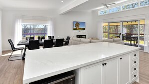 Een ruime woonkamer met een groot wit eiland, een eettafel met stoelen, een bank en een aan de muur bevestigde televisie.