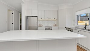 Een moderne keuken met witte kasten, een groot eiland, roestvrijstalen apparatuur en uitzicht op buiten.