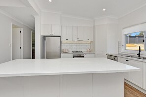 A modern kitchen with white cabinetry, a large island, stainless steel appliances, and a view of the outside.