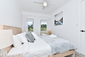 A bedroom with a bed, a ceiling fan, a window with a view of greenery, and a door. - Magpie 3 Two for Joy Estate (North Rothbury)