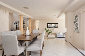 A spacious dining area with a wooden table and chairs, a staircase, and a living area with a sofa and a plant. - The Valley Way Luxury Estate (Mardi)
