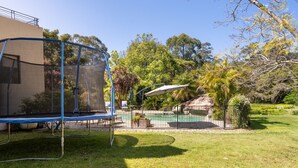 Un patio trasero con un trampolín, una piscina y un área cercada con árboles y arbustos.