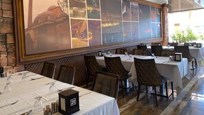 A restaurant with multiple tables, a large framed artwork on the wall, and a view of a cityscape. - Koç Otel Çankırı (Cankiri)