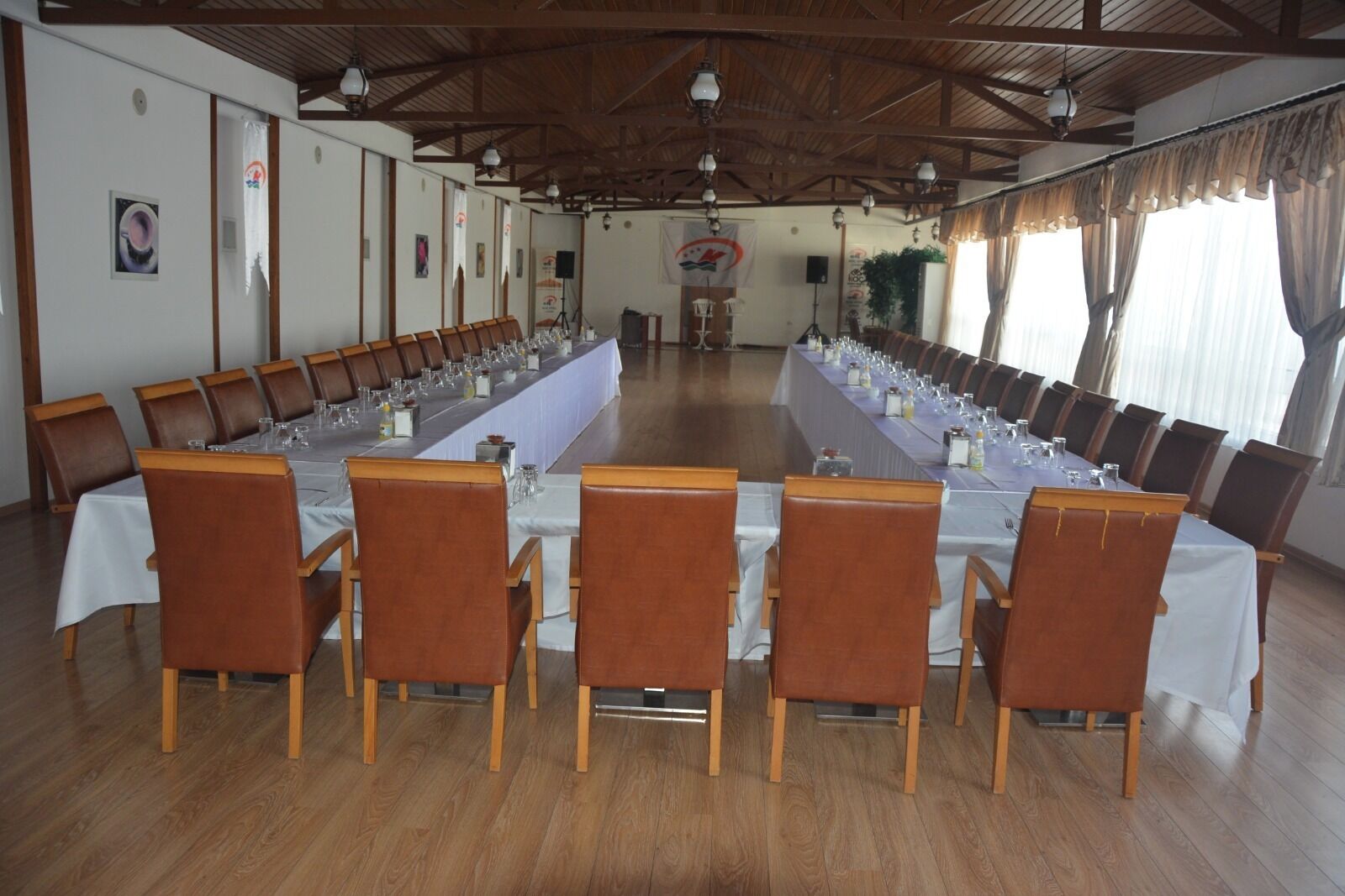 A conference room with long tables, wooden chairs, and a high ceiling with wooden beams.