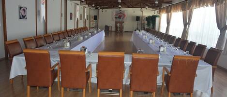 A conference room with long tables, wooden chairs, and a high ceiling with wooden beams.