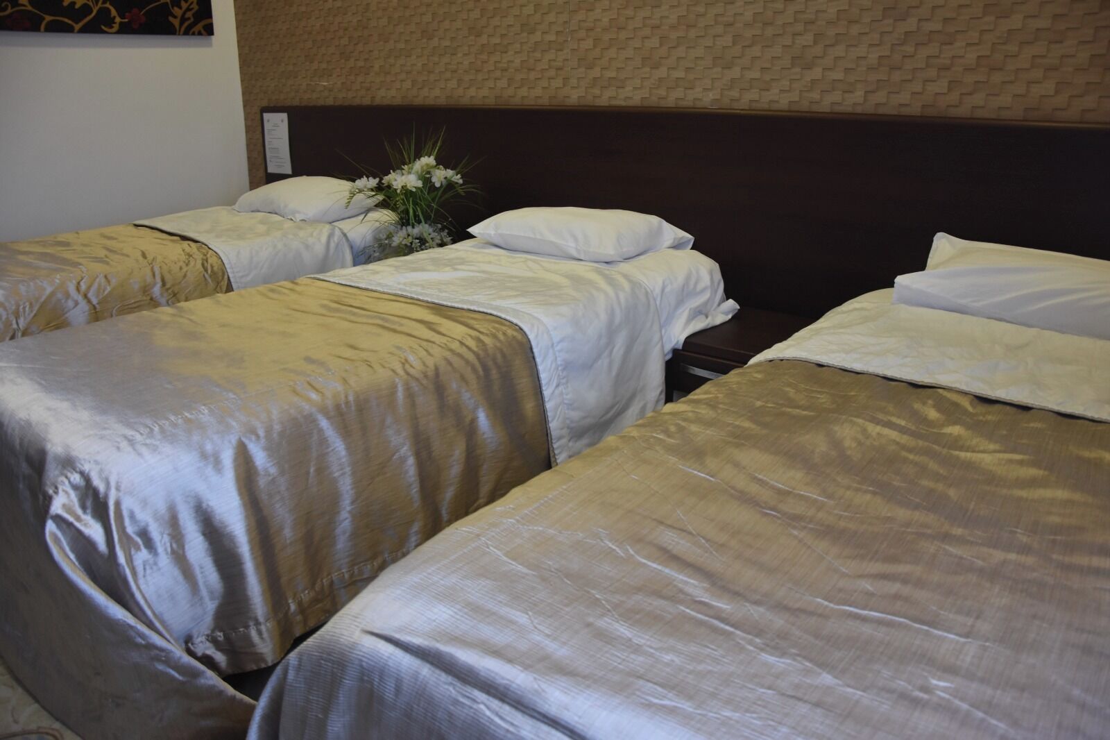 A hotel room with three single beds, each with a beige bedspread and white pillows.