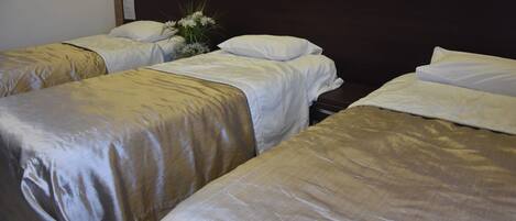 A hotel room with three single beds, each with a beige bedspread and white pillows.