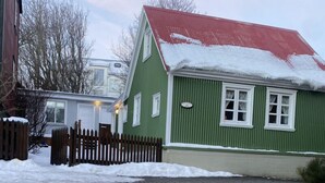 A green house with a red roof and a wooden fence in front.
