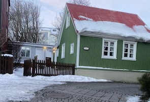 A green house with a red roof and a wooden fence in front.