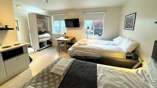 A compact hotel room with two beds, a kitchenette, a small dining table, and a TV.