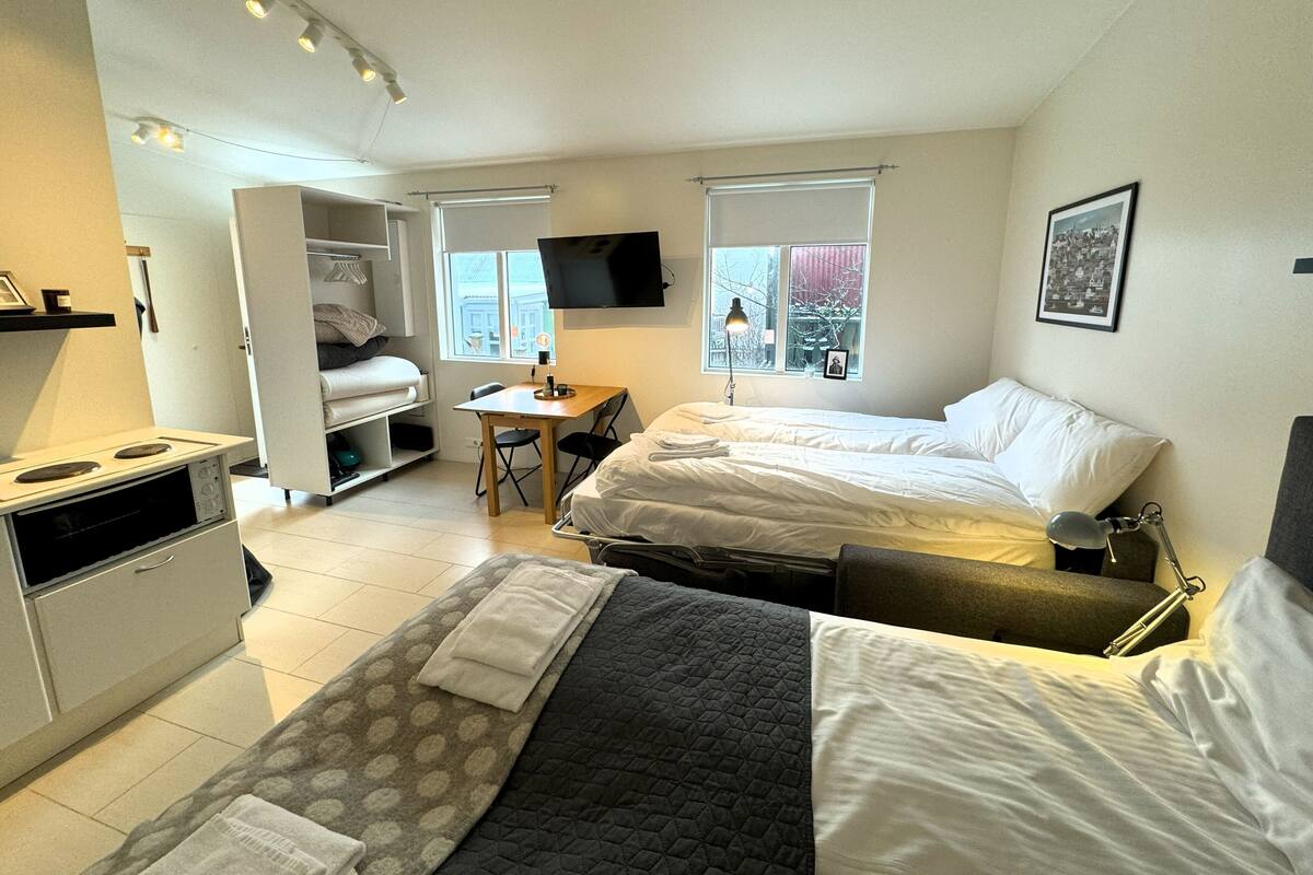 Una habitación de hotel compacta con dos camas, una kitchenette, una pequeña mesa de comedor y un televisor.