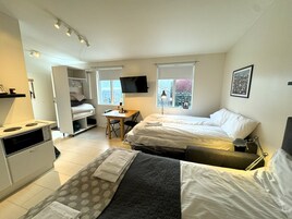 A compact hotel room with two beds, a kitchenette, a small dining table, and a TV.