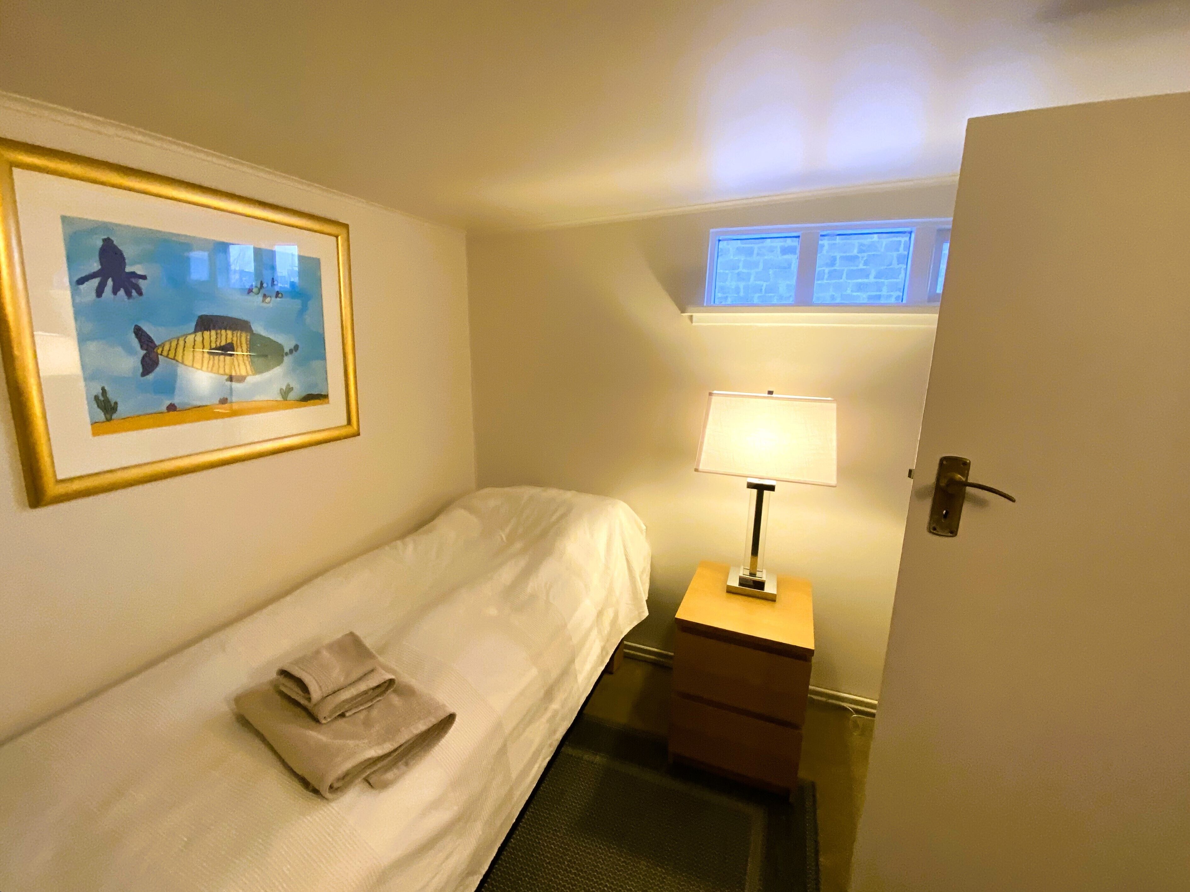 A hotel room with a bed, a nightstand with a lamp, a framed picture on the wall, and a window with a view.