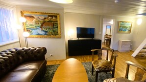 A living room with a leather sofa, a wooden coffee table, a flat-screen TV, and a painting on the wall.