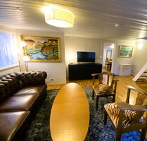 A living room with a leather sofa, a wooden coffee table, a flat-screen TV, and a painting on the wall.