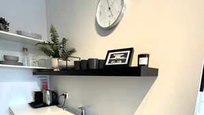 A modern kitchen with a white countertop, two burners, a stainless steel sink, and a clock on the wall.