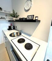 A modern kitchen with a white countertop, two burners, a stainless steel sink, and a clock on the wall.