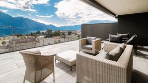 A balcony with wicker furniture, a view of a lake, and mountains in the distance.