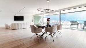 A modern living room with a glass dining table, white sofas, and a large window with a city view.