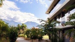 A modern building with a gravel pathway, surrounded by lush greenery and mountains in the background.