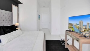 Habitación de hotel moderna con una cama grande, un televisor sobre un soporte de madera y vistas a la ciudad.