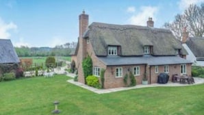 A traditional thatched-roof house with a well-maintained lawn and a small garden area.