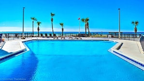 Une piscine d’un bleu éclatant, bordée de chaises longues et entourée de palmiers, le tout délimité par une clôture noire.