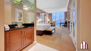 Une chambre d’hôtel équipée d’un lit, d’un bureau, d’une chaise, d’une grande fenêtre et d’une kitchenette.