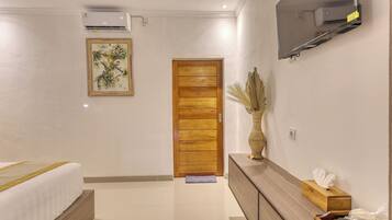 Una habitación de hotel moderna con una cama, una puerta de madera, un televisor montado y un jarrón con plantas secas.