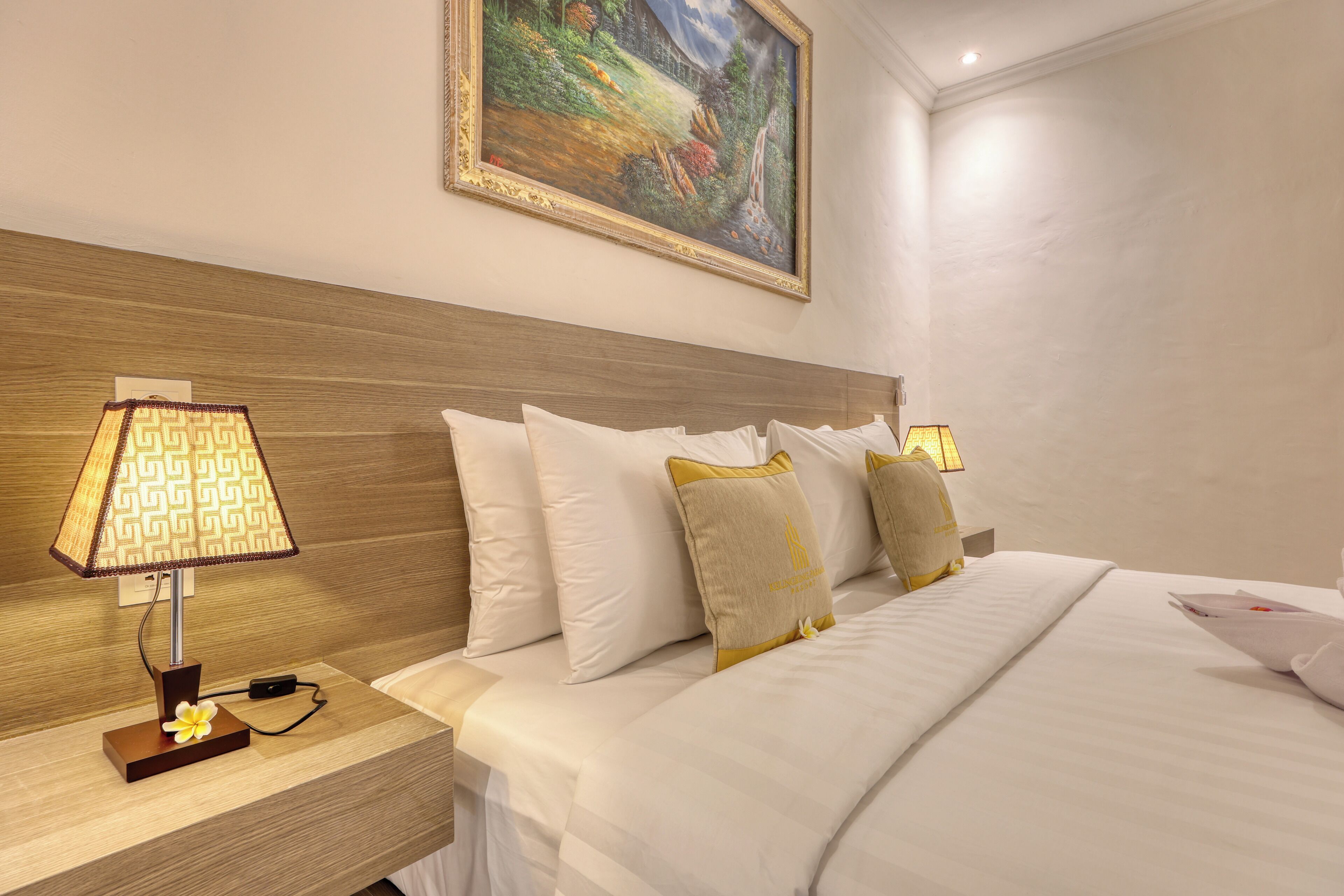 A hotel room with a neatly made bed, a nightstand with a lamp, and a painting on the wall.