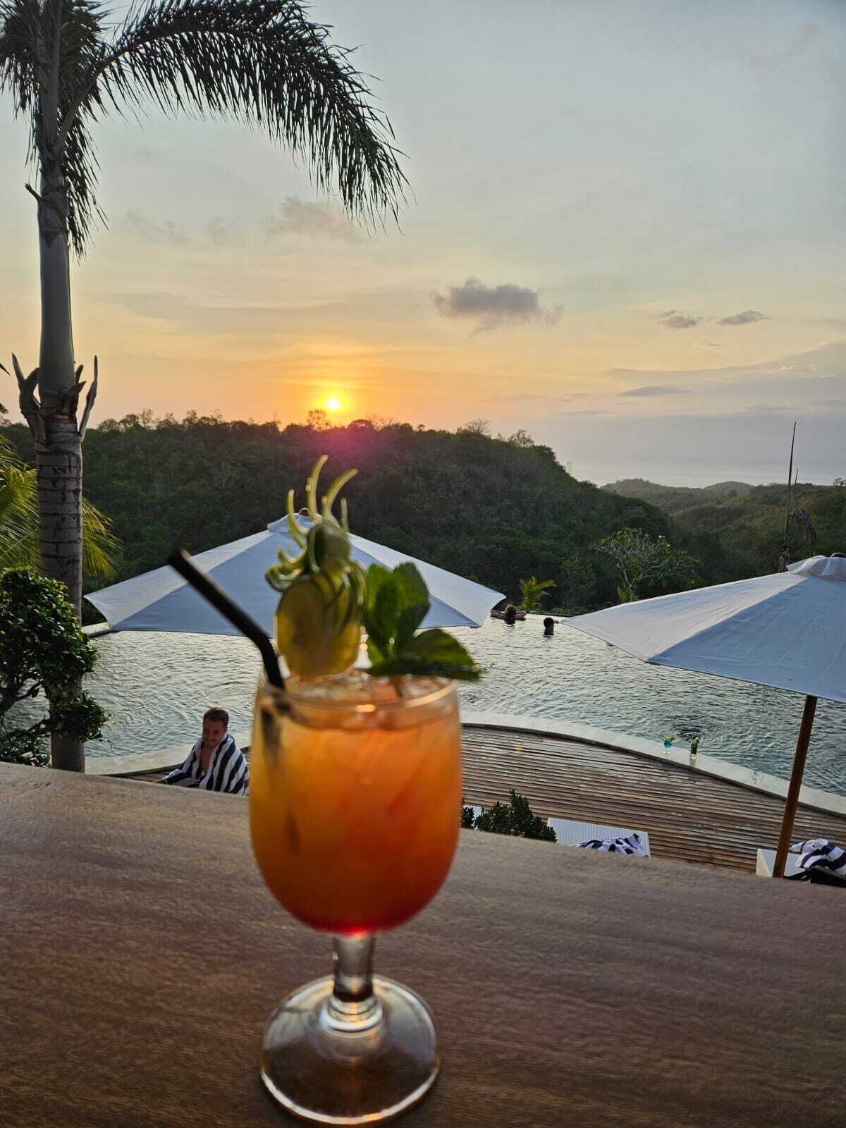 A sunset view from a balcony with a drink in a glass.