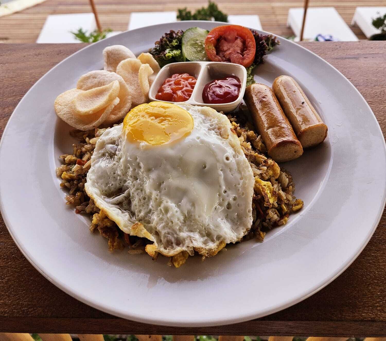 A plate with fried rice, a fried egg, sausages, and a side salad.