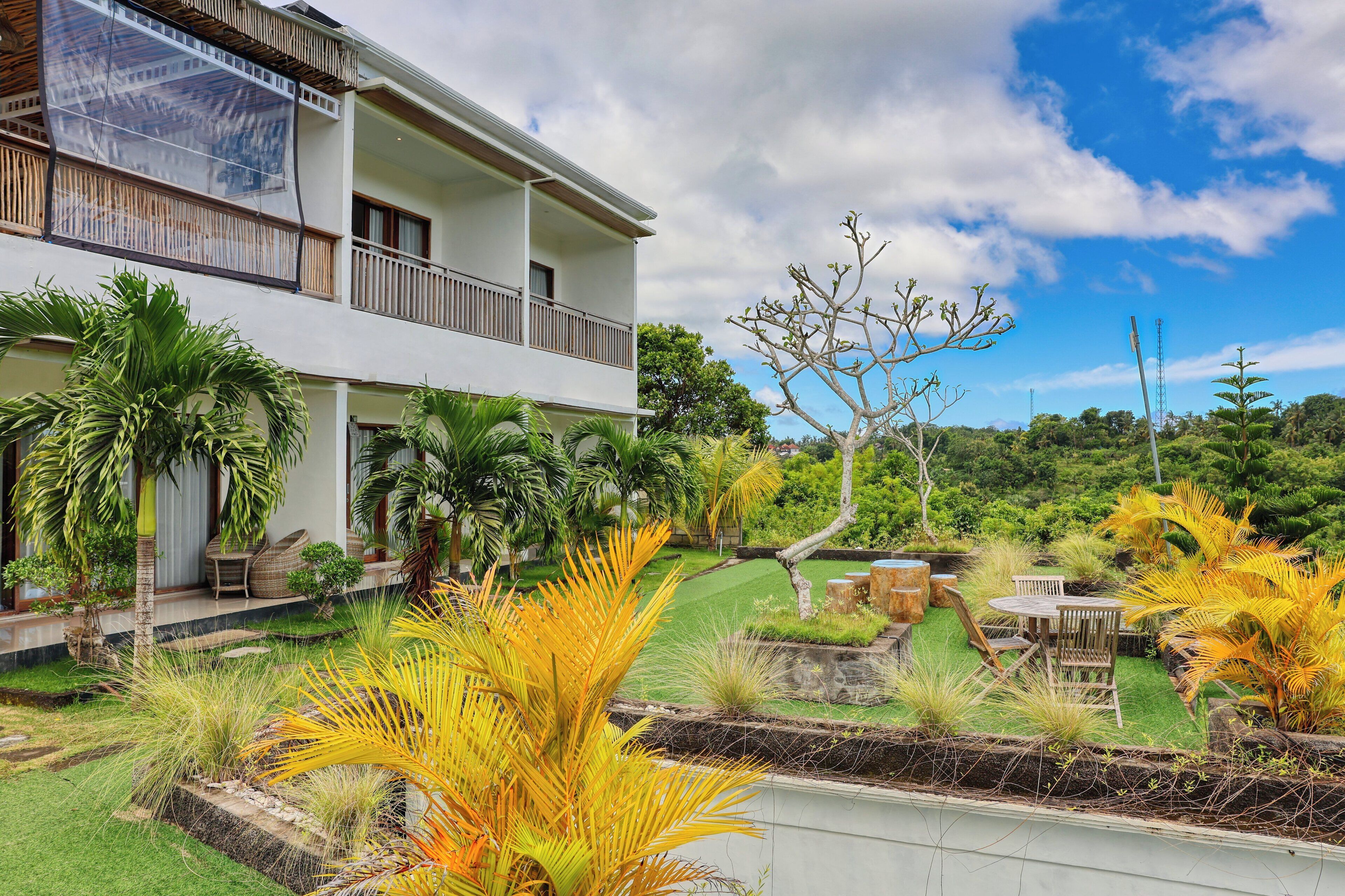 A two-story building with a balcony, surrounded by lush greenery and a well-maintained garden.