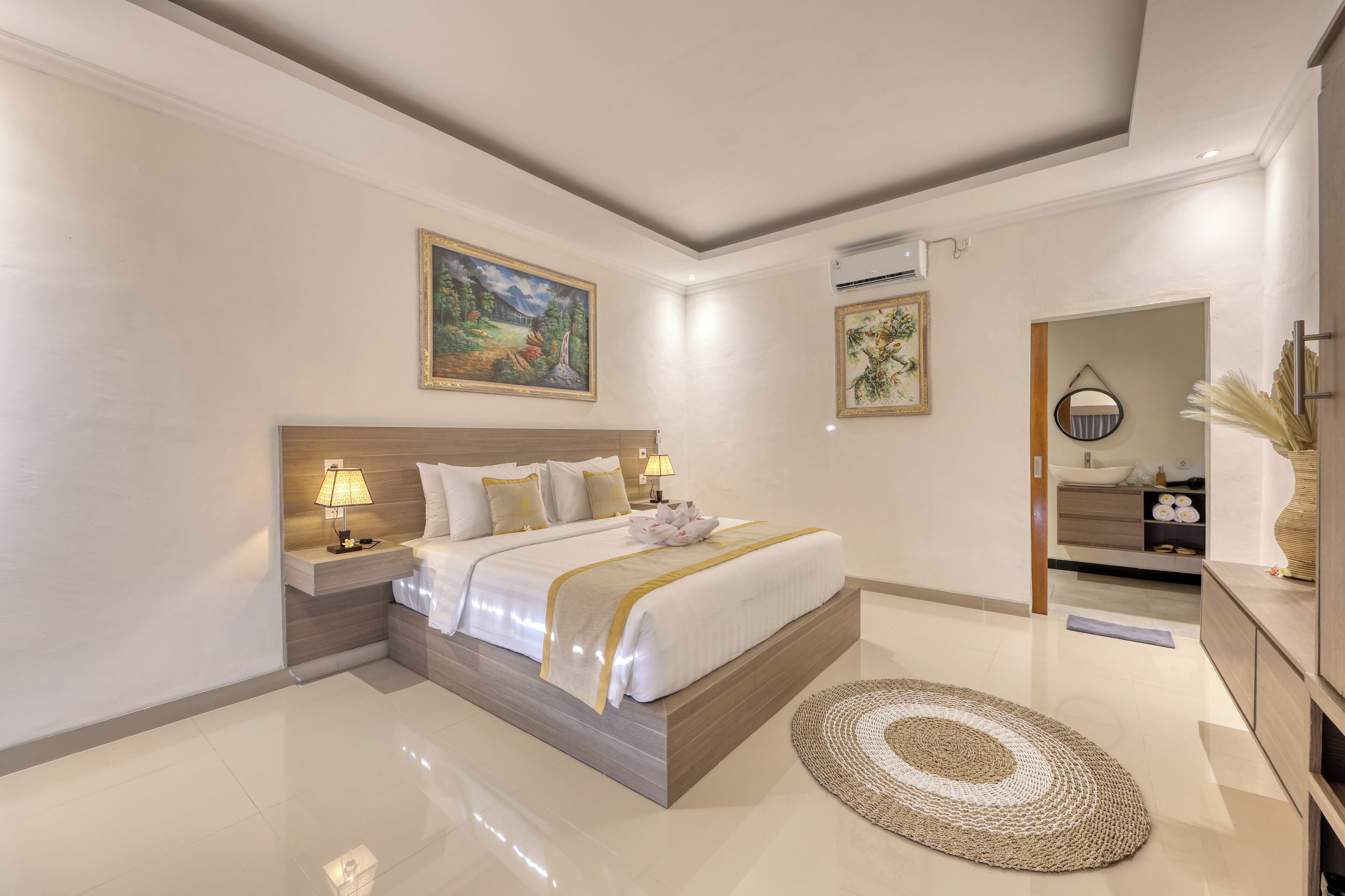 A modern hotel room with a large bed, bedside lamps, a round rug, and artwork on the walls.