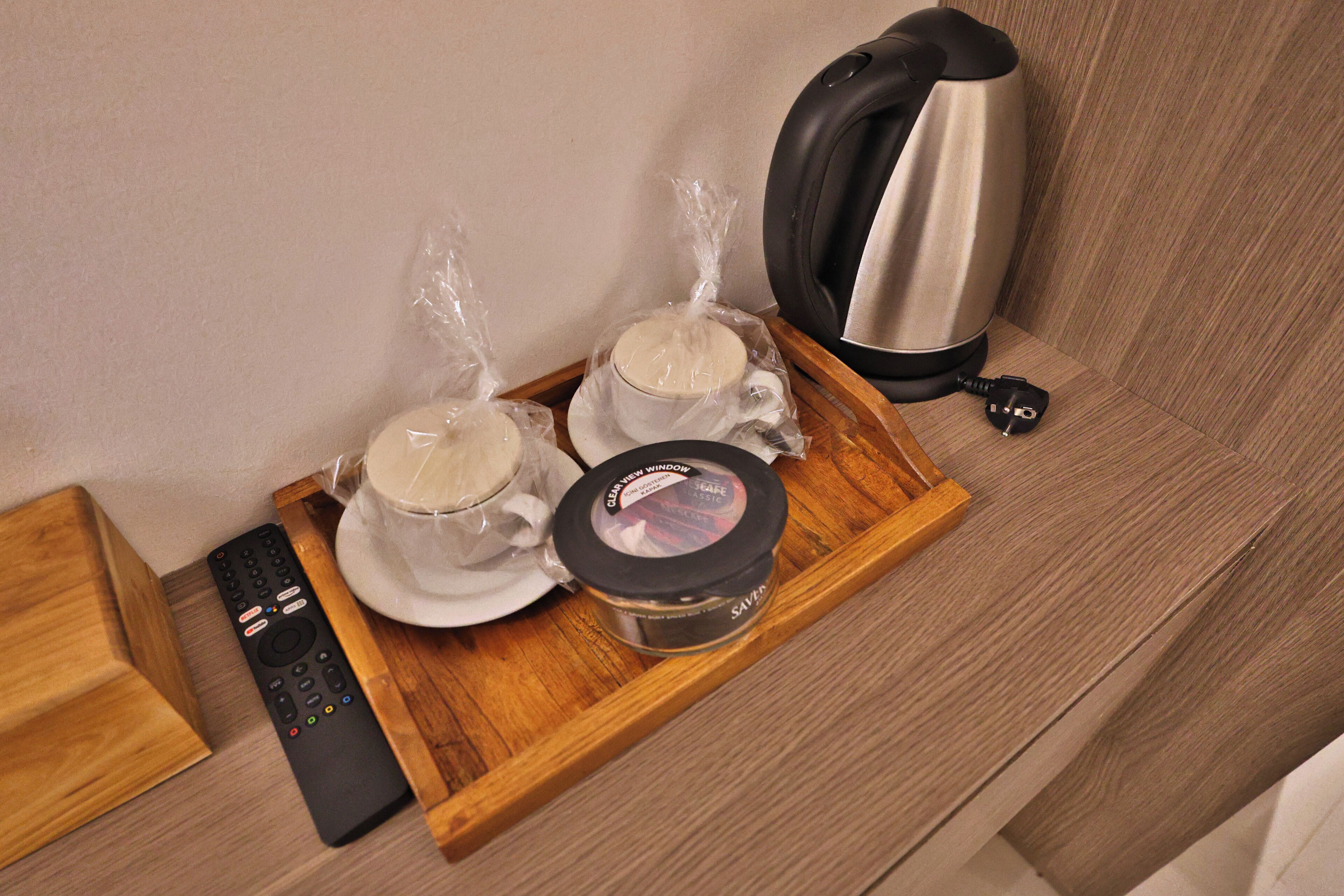 A tray with two cups, a kettle, and a remote control on a wooden surface.