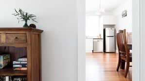 A modern kitchen with white cabinets, a stainless steel refrigerator, and a wooden dining table with chairs. - The Basin Cottage - Closest Home to The Gorge (West Launceston)