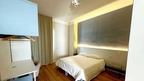 Moderni hotellihuone, jossa on sänky, työpöytä, tuoli ja suuri ikkuna.