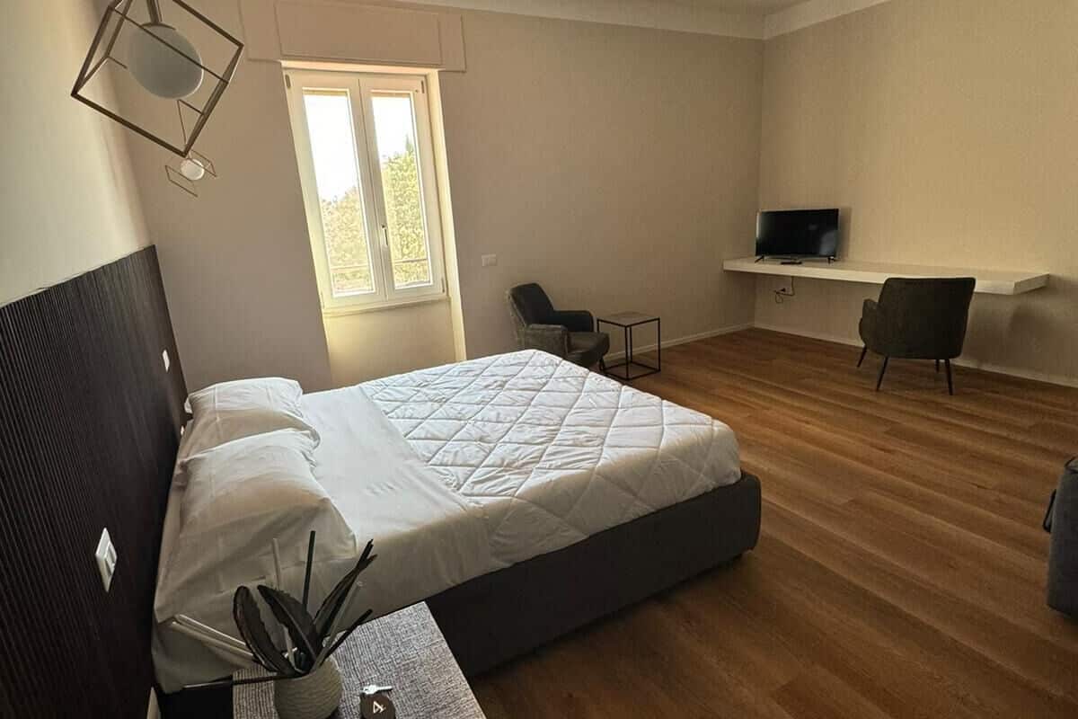 A modern bedroom with a bed, a desk, a chair, and a TV on a shelf.