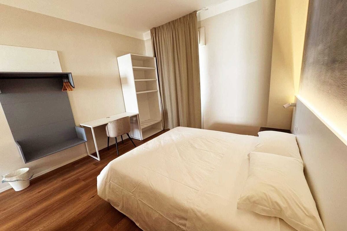 A hotel room with a bed, a desk, a chair, a wardrobe, and a curtain.