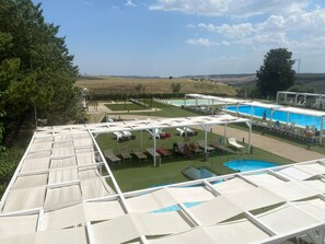 A pool area with multiple sun loungers and umbrellas, surrounded by a grassy landscape and a clear sky. - Tenuta Lo Cuoccio (Gravina in Puglia)