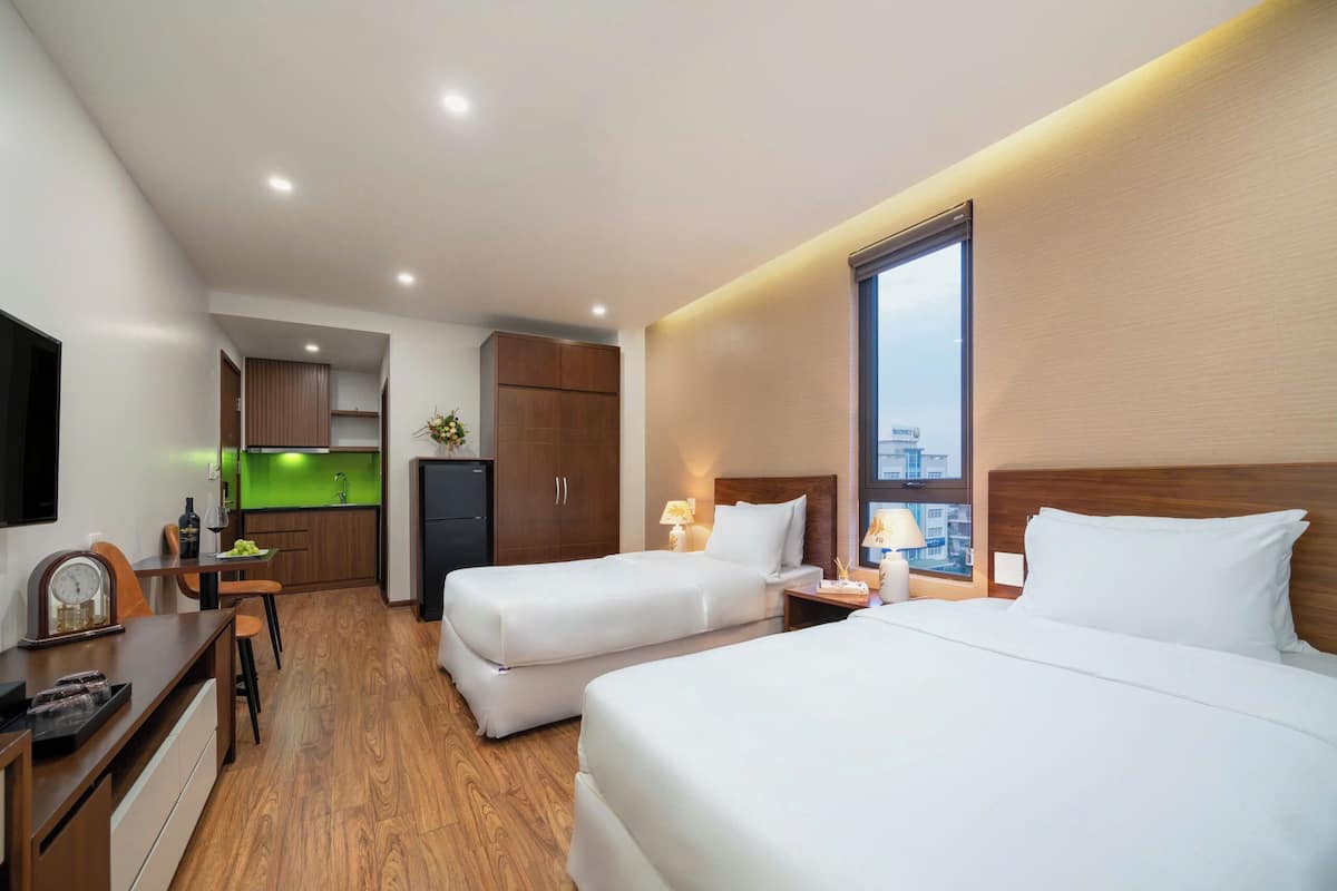Hotellihuone, jossa on kaksi sänkyä, pieni keittonurkkaus ja näkymä kaupunkiin.