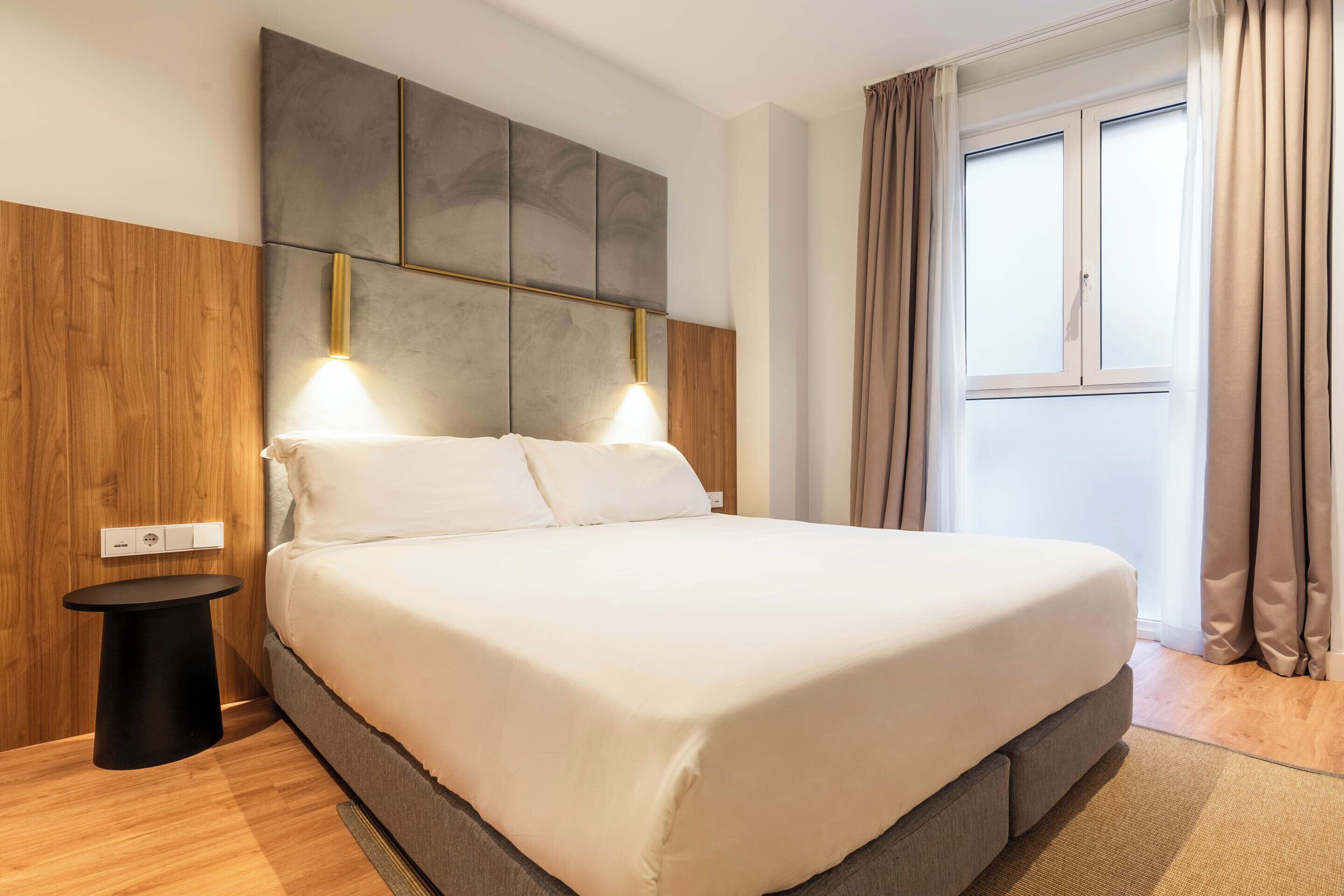 Una moderna camera d'albergo con un letto grande, una parete d'accento in legno, un piccolo tavolino e una finestra con tende.