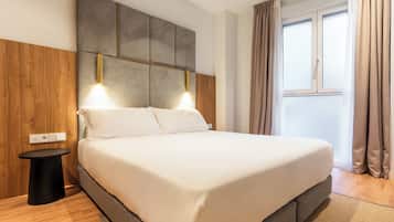 Una moderna camera d'albergo con un letto grande, una parete d'accento in legno, un piccolo tavolino e una finestra con tende.